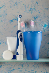 Manual toothbrushes stand in a glass, next to an electric brush, on shelf