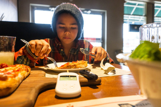 Child with diabetes in a restaurant eating, a glaucometer and lancet are on the table.