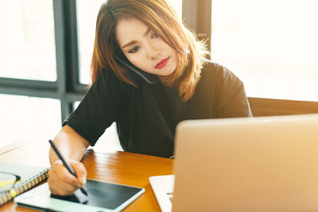 Asian stylish woman designer wear black dress and red lips using smartphone while working with her laptop in selective focus..