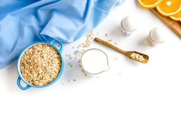 Oat flakes plate with milk, orange, eggs on a wooden white table. Top view of healthy oat flakes breakfast. Copy space. blue napkin Breakfast in bed plate, breakfast table buffet. Healthy ingredients.