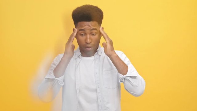Young african man in shirt having throbbing headache and touching his temples over yellow background