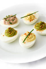 Variety of stuffed eggs with avocado and tuna  in plate isolated on white background