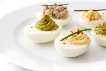 Variety of stuffed eggs with avocado and tuna  in plate isolated on white background