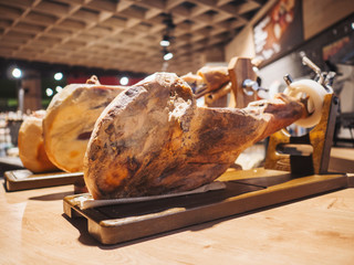 Pork leg on table. Jamon serrano. Traditional Spanish ham in restaurant or store interior. Whole jamon on stand. Selective focus. Gourmet ham. Shallow DOF. Copy space.