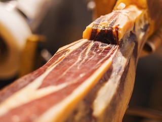 Jamon serrano. Traditional Spanish ham in the market close up. Pork leg ham on table. Meat in restaurant interior. Whole jamon on stand. Selective focus. Gourmet ham. Shallow DOF. Copy space.