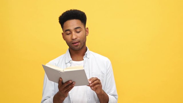 Disappointed Young african man in shirt reading book over yellow background