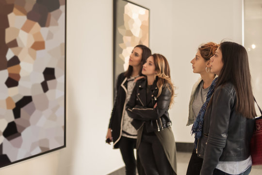Four girl friends looking at modern painting in art gallery