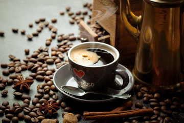 Black coffee in a cup on the table in a composition with coffee accessories on an old background
