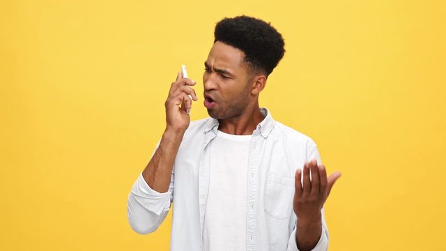 Serious Young african man in shirt quarrels by smartphone over yellow background