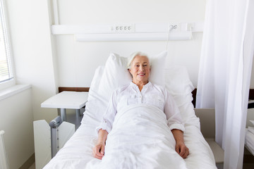 smiling senior woman lying on bed at hospital ward