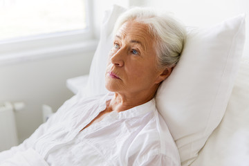 sad senior woman lying on bed at hospital ward