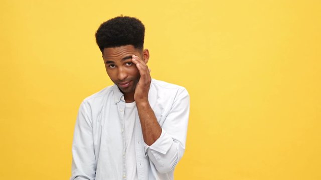 Young african man in shirt talking with somebody and covering his face over yellow background