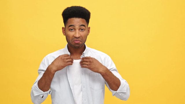 Young african man in shirt corrects his appearance over yellow background