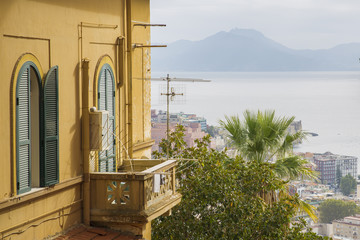 Fototapeta na wymiar Panorama del golfo di Napoli dal quartiere collinare Vomero. In primo piano un palazzo con una finestra chiusa copre parzialmente la vista