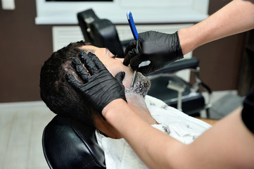 Hairdresser shaves man's beard with a blade in a male barber shop