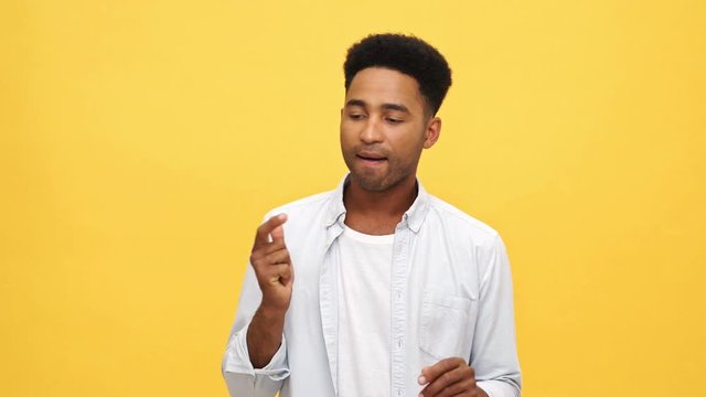 Smiling african man in shirt recounts something on his fingers and looking at the camera after that over yellow background