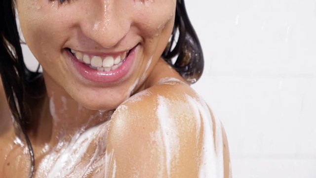 Woman cleaning skin with sponge in shower pan from shoulder to face smiling