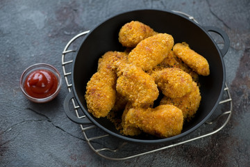 Cast-iron pan with roasted breaded chicken wings on a metal cooling rack, textured asphalt background, studio shot