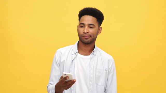 Displeased african man in shirt talking by smartphone over yellow background