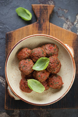Bowl with baked beef meatballs in tomato sauce on a rustic wooden serving board, view from above