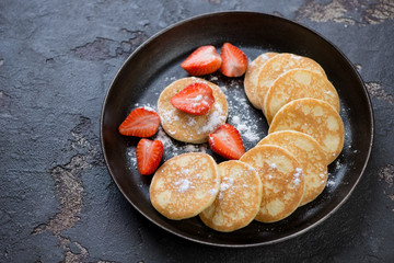 Metal plate with fritters served with fresh strawberry and powdered sugar, studio shot