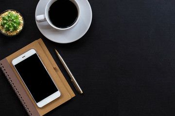Office desk with smartphone, notepad, hot coffee and plant. Top view of black office desk with copy space. Business desk minimal style concept.