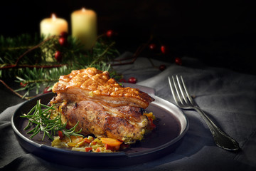 festive roast pork meal with crispy crust on a gray plate, tablecloth, christmas decoration and candles against a dark background with copy space