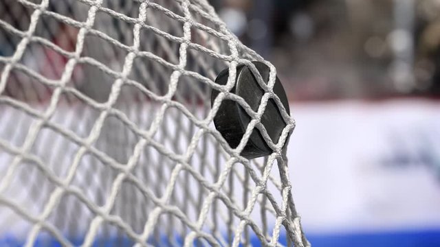 Hockey puck flies into the net on a hockey boards with a blue stripe. In slow motion