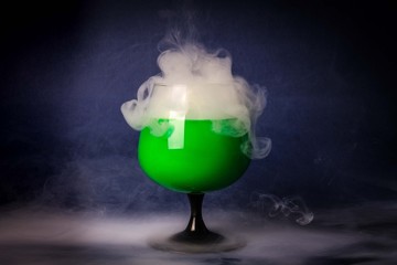 Smoke into cocktail glass on a black background. Witch potion background for Halloween. Unusual bar drink.