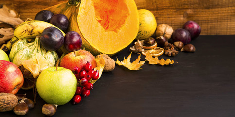 Fall fruits and vegetables harvesting on wooden tray, pumpkins, apples, plums, walnuts and chestnuts, fall decoration on wooden background