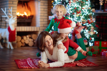 Family with kids at Christmas tree and fireplace.