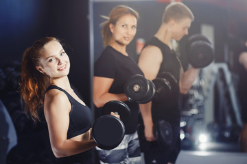 Fototapeta na wymiar Team of friends of the girl and the guy are engaged in the gym with dumbbells. Concept sport, training