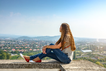The girl sits on the edge of the fortress and looks at the city from a height.