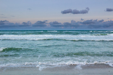 Sea waves rolling on empty sandy beach, stormy cloudy sunrise