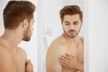Young man applying cream onto skin in bathroom