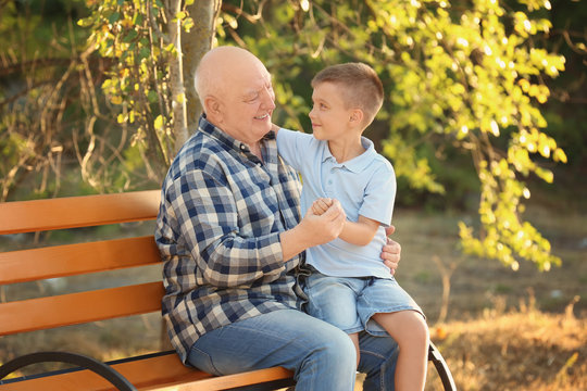 Happy senior man with grandson sitting on bench in park