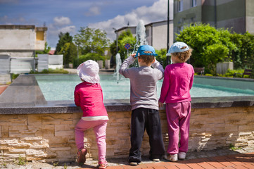 Zdjęcie od tyłu dzieci patrzących w fontannę. Zdjęcie latem.