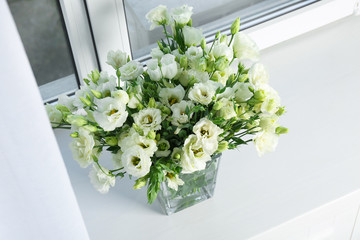 Vase with beautiful eustoma flowers on window sill