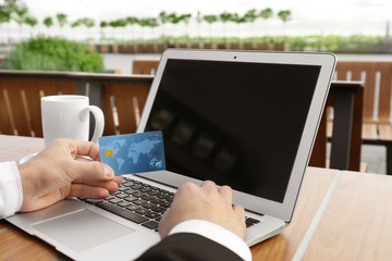 Young man using laptop and credit card for online shopping at table