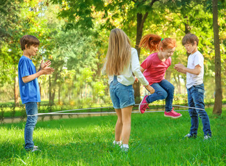 Fototapeta na wymiar Cute little children jumping rope in park