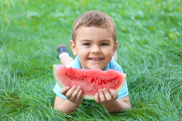 Cute boy eating watermelon on green grass