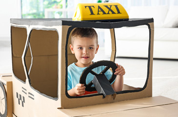 Little boy playing with cardboard taxi in light room