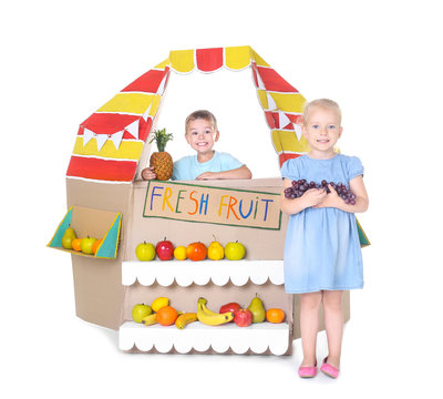 Little children playing with cardboard stall on white background