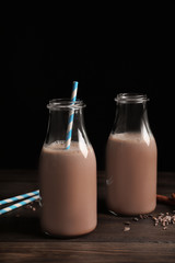 Bottles with yummy cocoa on wooden table against black background