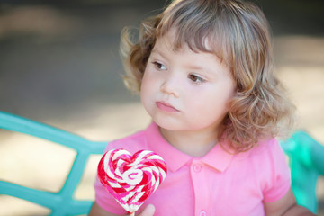 Beautiful little girl holding a big heart shaped lollipop.