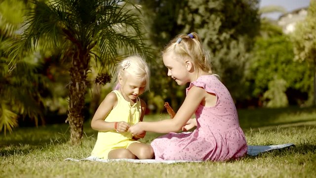 two cheerful little sisters are sitting on a grass and playing in a garden in summer vacation