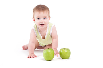 Fototapeta na wymiar cute beautiful baby boy in green shirt stand on all fours near green apples
