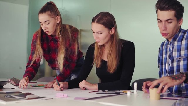 Group of young interior designers team working together in creative office. Young professionals making sketches sitting at the table, preparing their new project and drinking coffee in slowmotion