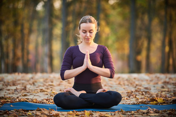 Beautiful young woman meditates in yoga asana Padmasana - Lotus pose on the wooden deck in the...