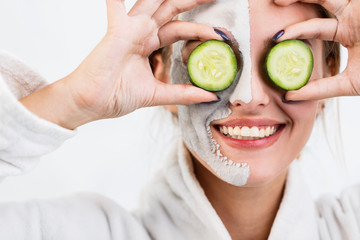 Smiling girl having fun with two pieces of cucumbers during face care, isolated shot in the white background